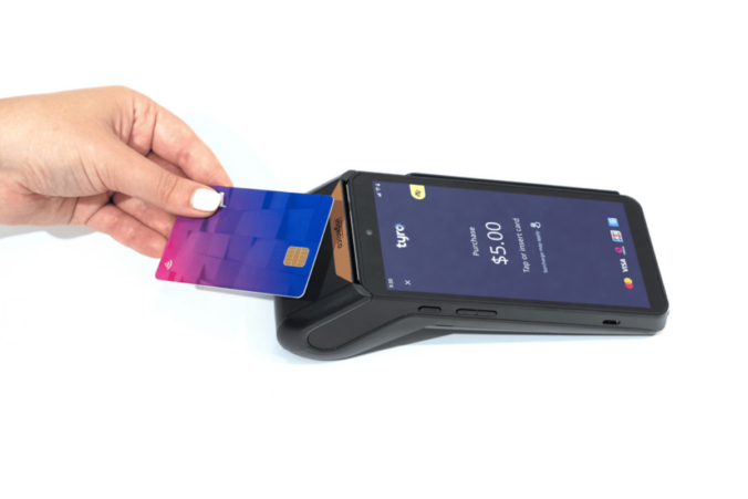 A person holding a credit card to a mobile phone for payment using a Tyro EFTPOS machine.